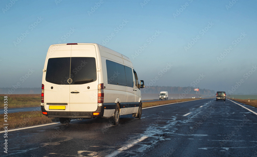 A white minibus transports people to another city on a wet highway. The concept of passenger transportation on minibuses, international, copy space A white minibus transports people to another city on a wet highway. The concept of passenger transportation on minibuses, international, copy space