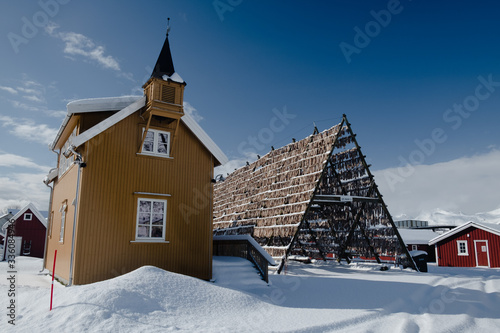 Yellow house in scandinavian style with a belfry. Drying rack is fully hanged by famous stockfish. Winter photo shows symbols of faith and fishery which are very important for Norwegian culture. photo