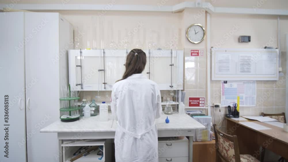 Female scientist analyzes liquid in distillery laboratory researcher. Woman stands with her back to camera. Mixing chemicals and alcoholic beverage. Female scientist analyzes liquid in distillery laboratory researcher. Woman stands with her back to camera. Mixing chemicals and alcoholic beverage.
