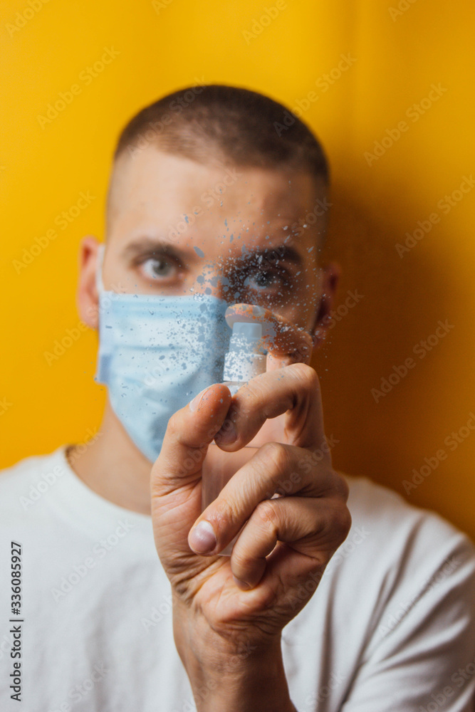 Portrait of a young guy in a mask on a yellow background. Disinfects hands with an antiseptic. Sprays the pest control. The concept of coronavirus. Protection against germs and viruses. Portrait of a young guy in a mask on a yellow background. Disinfects hands with an antiseptic. Sprays the pest control. The concept of coronavirus. Protection against germs and viruses.