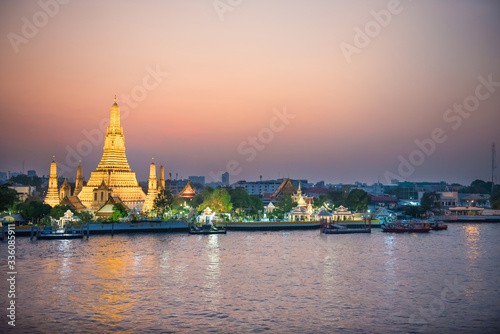 Illuminated Temple of Dawn or Wat Arun and Thonburi west bank of Chao Phraya River at sunset. Bangkok, Thailand