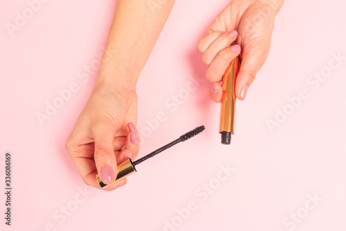  Beautiful young woman s hands holding  mascara on pastel pink background .