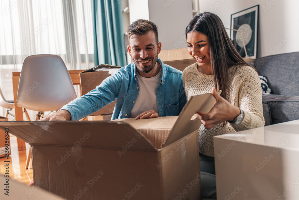 Smiling young couple move into a new home sitting on floor and unpacking boxes of their belongings. Smiling young couple move into a new home sitting on floor and unpacking boxes of their belongings.