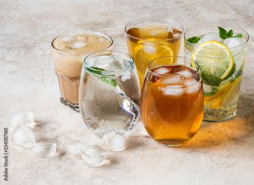 Various refreshing drinks in glasses with ice. Apple juice, homemade lemonade, iced coffee, iced fruit tea and sparkling water on beige background.