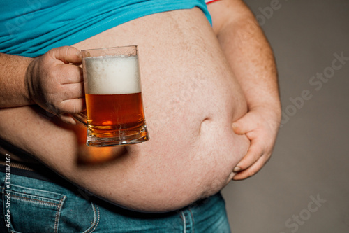 A man with a fat belly holding a glass of beer. On dark background.