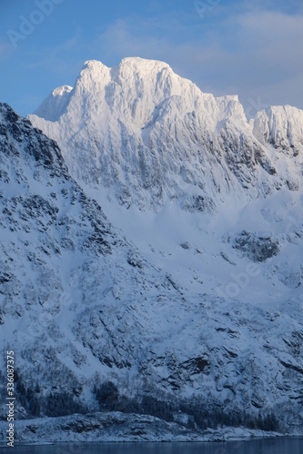 Beautiful mountain massif spotted during the sunset.  Sunshine is touching snowy and frosty summit. This amazing winter landscape is located close to Svolvaer city in Lofoten Islands.