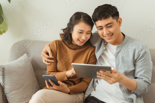 leisure, technology and internet addiction concept - happy couple with tablet computer and smartphone at home