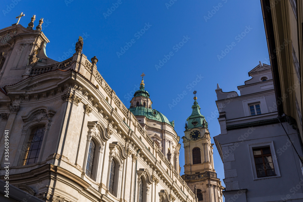 view of the facades of historical Prague buildings, cream colored ornate facades, and green domed roofs, clear blue sky