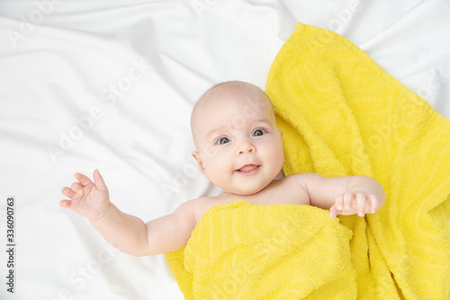 Portrait of a beautiful cheerful baby in a yellow towel after bath on a white cloth