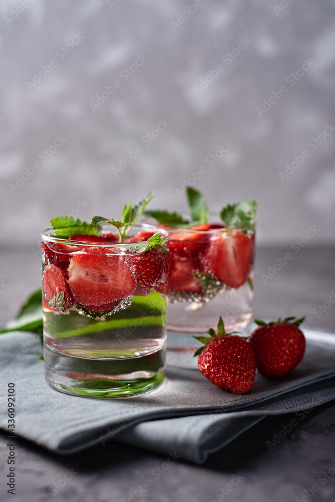Water with strawberry and mint in sparkling glasses on gray napkin on concrete table, copy space. Cold summer drink. Mineral water Water with strawberry and mint in sparkling glasses on gray napkin on concrete table, copy space. Cold summer drink. Mineral water