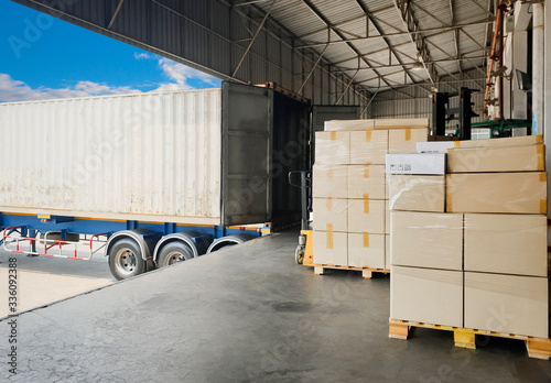 Interior of Distribution Warehouse. Stacked of Package Boxes Load with Cargo Container. Trailer Truck Parked Loading at Dock Warehouse. Shipping Warehouse Logistics. Freight Truck Transportation.