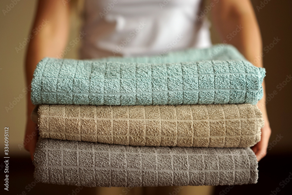 A woman holds a pile of multicolored neutral terry towels in her both hands ready for cleaning and organizing A woman holds a pile of multicolored neutral terry towels in her both hands ready for cleaning and organizing