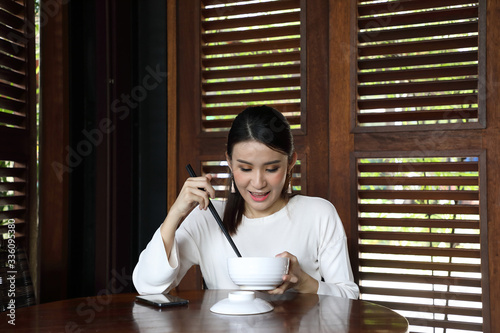 Young asian woman sit at rustic cafe eat from chinese chopsticks from soup noodle from bowl look down at food