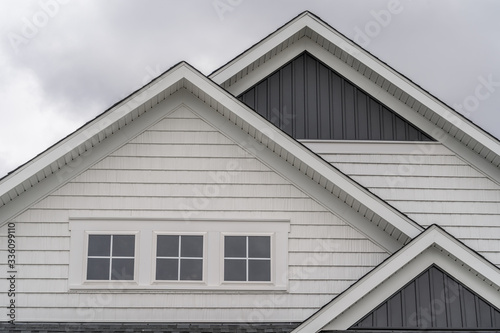 Triple gable facade with thick white frame triple attic window, white horizontal vinyl siding, dark vertical siding on a new construction East Coast American single family home
