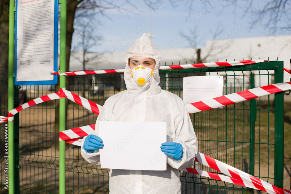 Obraz premium Osoba z białą kartką w dłoniach stojąca przed taśmami zabezpieczającymi wejście do parku w czasie pandemii