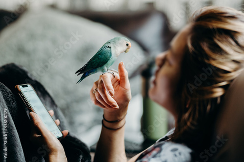 Woman liviing with Lovebird on hand with smart phone in livingroom. photo