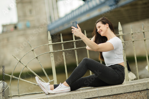 young woman sitting on a wwall taking a selfie photo