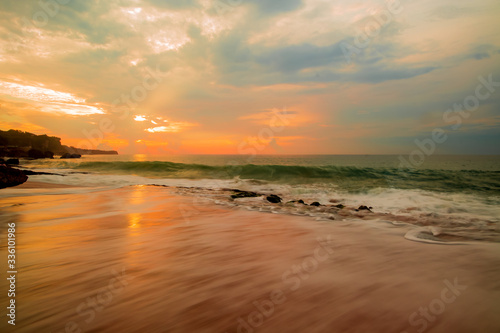 Seascape. Sunset time. Sunlight reflection. Beach with rocks. Ocean with motion blur waves. Slow shutter speed. Tegal Wangi beach, Bali, Indonesia