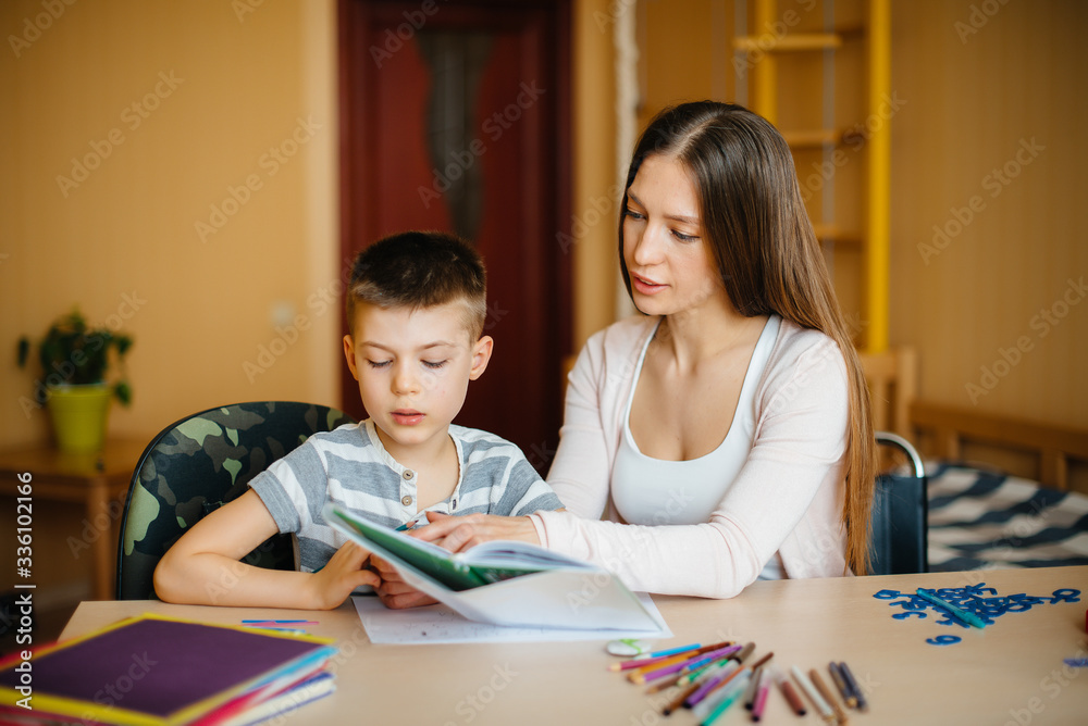 A young mother is doing homework with her son at home. Parents and training A young mother is doing homework with her son at home. Parents and training