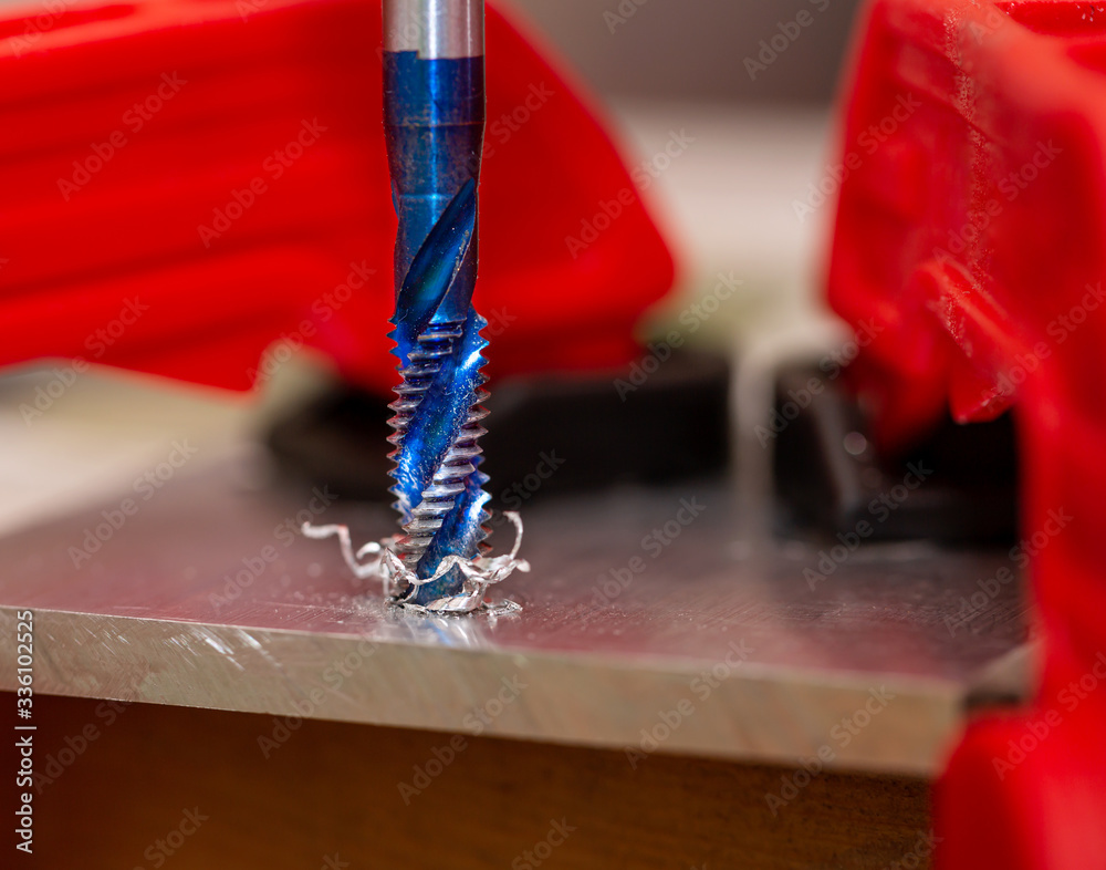 Manual cutting of thread in hole in the aluminum sheet closeup. Tapping