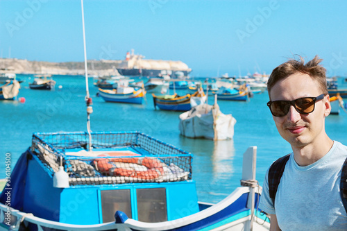 Marsaxlokk harbor fishing boats colourful Malta, Young man sitting at water front. Banner for a tourist company.  © frecca