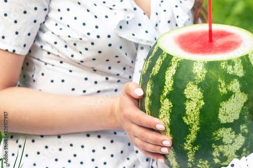 Girl holds whole watermelon with cocktail straw on green summer background.