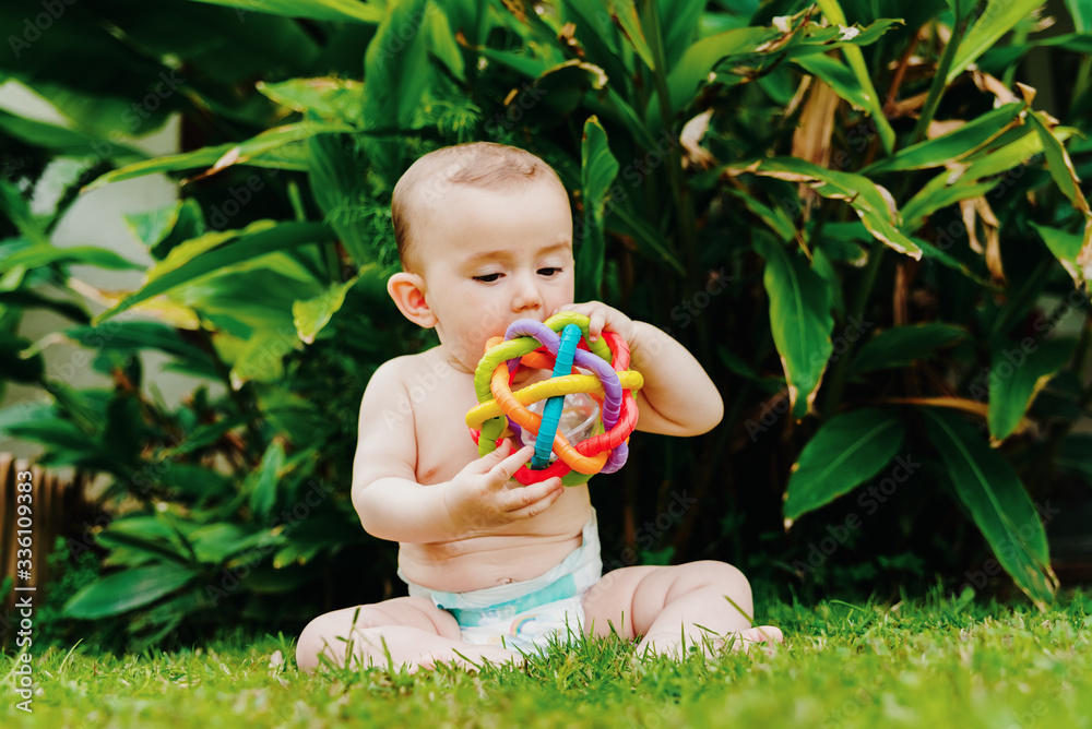 Baby sitting on the barefoot grass nibbling on a plastic toy. Baby sitting on the barefoot grass nibbling on a plastic toy.
