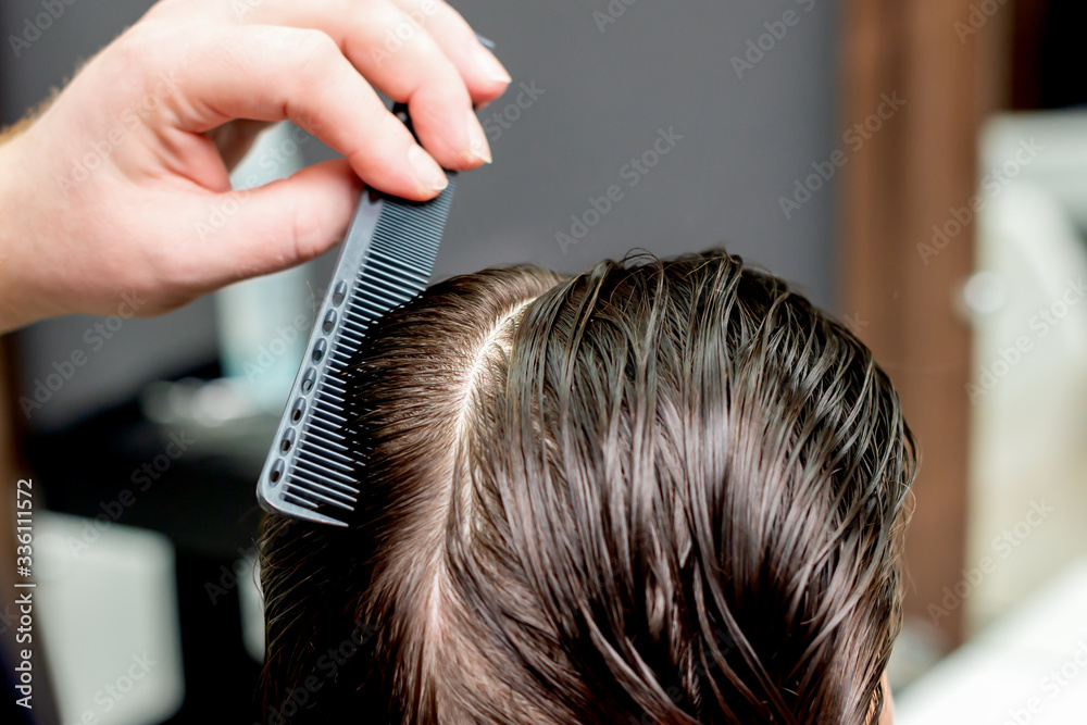 Fototapeta premium Hand of hairdresser combs wet hair of woman close up.