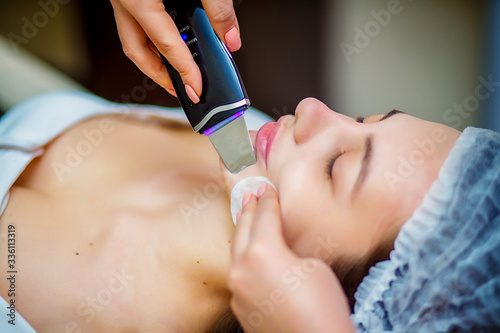 Woman receiving ultrasonic facial exfoliation at cosmetology salon. Procedure clearing clogged pores  ultrasonic treatment for skin rejuvenation  beautician uses modern apparatus for refreshing