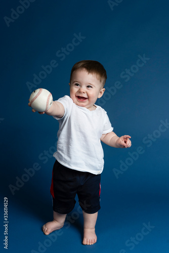 Happy baby boy on blue background holding a baseball