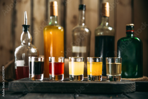 Variety of alcohol bevegares in shots and bottles behind on the black wooden board, side view, horizontal