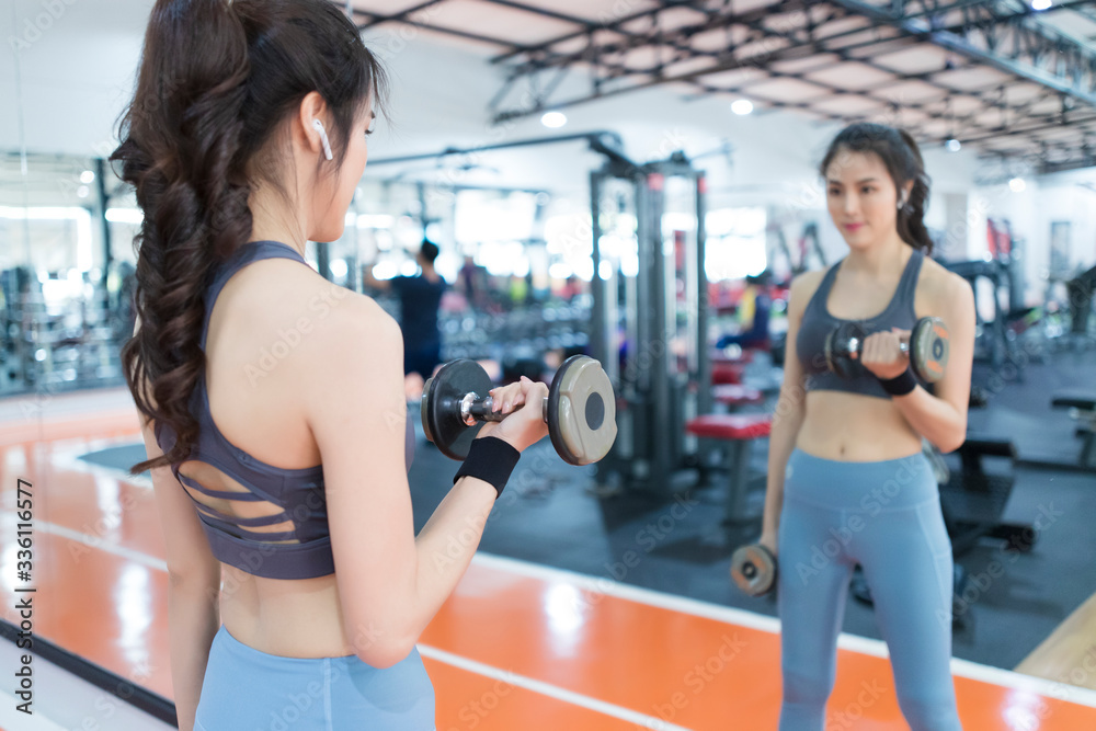 Fototapeta premium Asian woman lifting dumbbells in fitness room. Young woman lifting dumbbells in the gym.