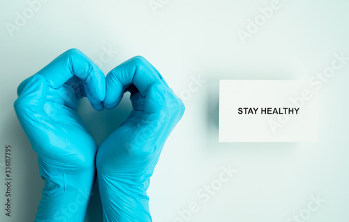 stay home and healthy to prevent covid-19 spread campaign, text on paper with heart shape hands of doctor wearing blue gloves