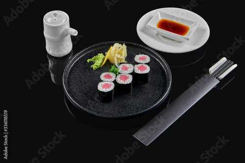 Traditional maki sushi rolls with tuna on a black plate in composition with soy sauce and chopsticks on a black background. Japanese food. Photo for the menu