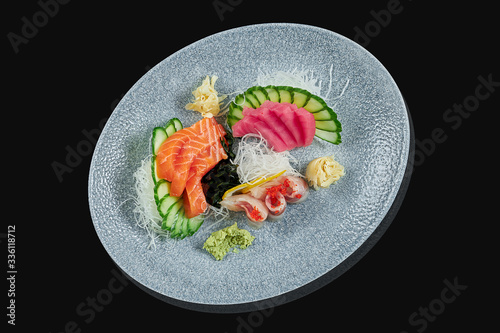 Classic raw set of sashimi salmon, seabass and tuna with cucumber and daicon on a stylish black ceramic plate on a black background. Japanese traditional food. Photo for the menu photo