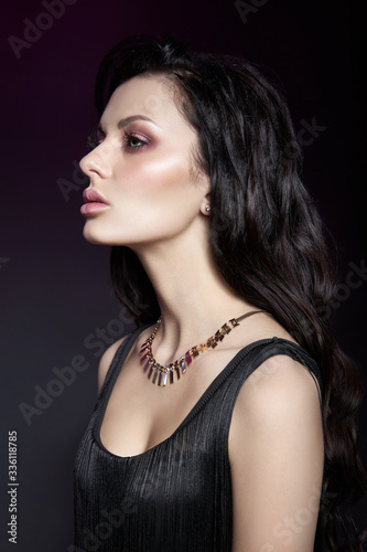 Portrait of a brunette woman with a chic hairstyle and a necklace around her neck, jewelry. Natural cosmetics and beautiful bright makeup on the face of the girl