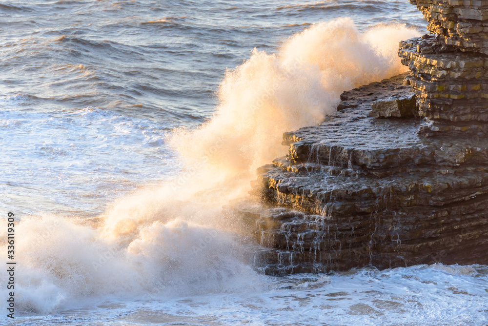 Waves crashing over a tiered rock formation.  