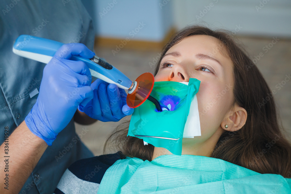 Dentist examining a patient's teeth in the dentist. Female dentist fixed and dry dental fillings with a light. The girl is sitting in a chair at the dentist's appointment. Dentist examining a patient's teeth in the dentist. Female dentist fixed and dry dental fillings with a light. The girl is sitting in a chair at the dentist's appointment.