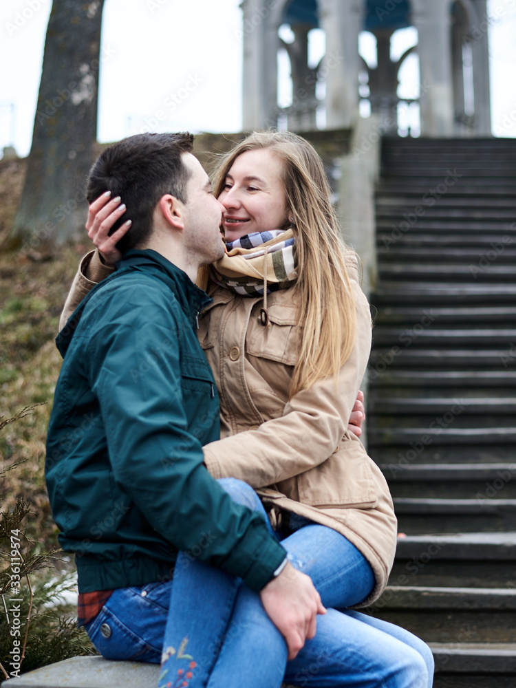 Young blond woman, is sitting on brunette man's lap, hugging each other and kissing on the old stairway. Romantic Valentines day celebration Young blond woman, is sitting on brunette man's lap, hugging each other and kissing on the old stairway. Romantic Valentines day celebration