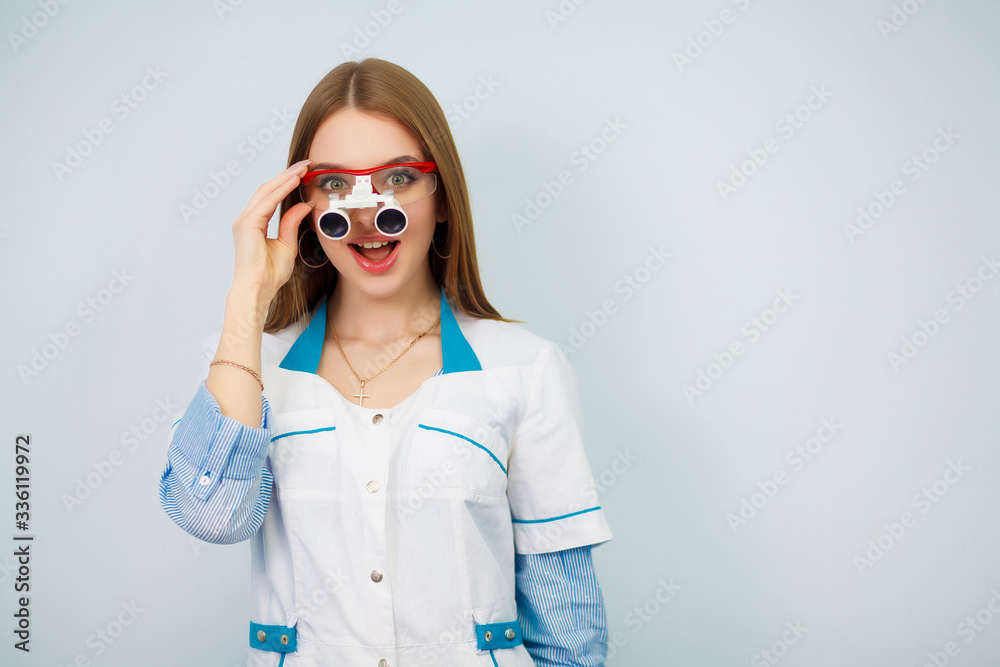 Portrait of young stomatologist making funny face while looking at camera and smiling. Copy space. Beautiful girl in a white coat. Portrait of young stomatologist making funny face while looking at camera and smiling. Copy space. Beautiful girl in a white coat.