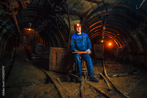 A miner in a coal mine stands near a trolley. Copy space. photo