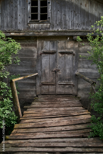 Old wooden grey hut in the village. Old time watermill among green trees in countryside. Doors of ancient wooden building 