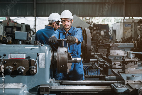 Engineer men wearing uniform safety workers perform maintenance in factory working machine lathe metal.
