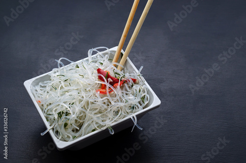 asian glass funchose noodles and bamboo sticks on a white square plate on a black slate background with place for text. oriental asian cuisine, veganism, lean food, flexitarianism, peganism, keto diet photo