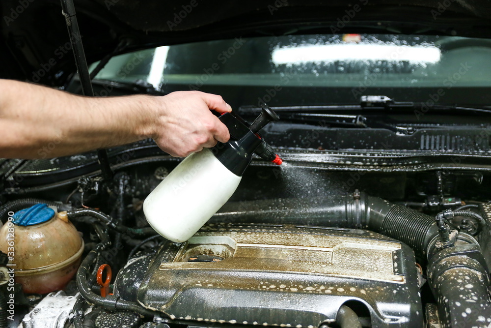 car engine washing closeup. car wash worker apply detergent on car