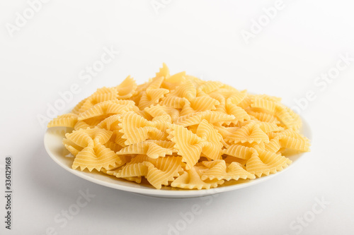Dried Farfalle Rigate Italian pasta on a plate ready to be cooked, isolated on a white table, top view or flat lay of healthy food 