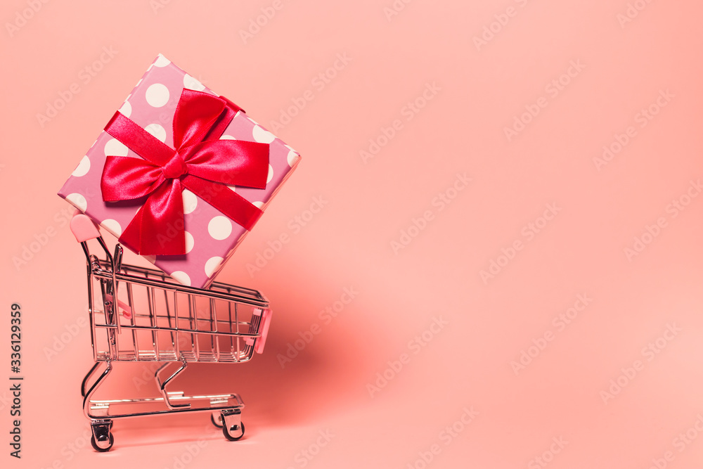 Small decorative trolley with present box on bright colorful background. Christmas or birthday gift. Sales and shopping concept. Small decorative trolley with present box on bright colorful background. Christmas or birthday gift. Sales and shopping concept.