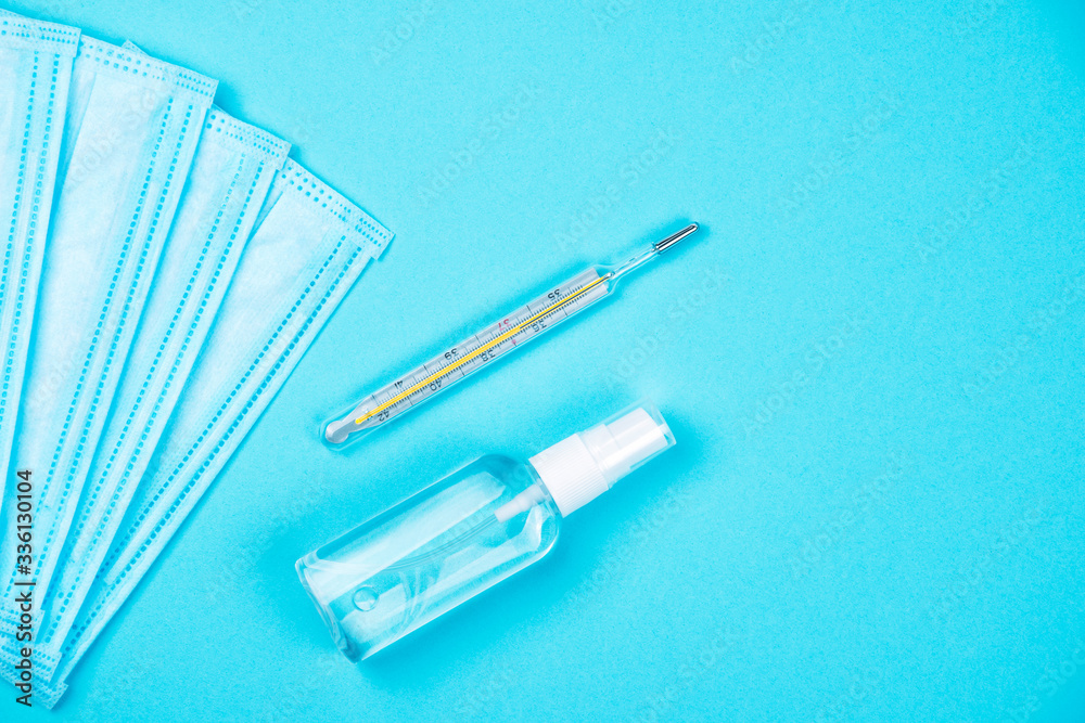 Top view of two disposable medical surgical protective face mask with antibacterial antiseptic spray for hands sanitizer and thermometer on blue background. Protection against virus. Copy space Top view of two disposable medical surgical protective face mask with antibacterial antiseptic spray for hands sanitizer and thermometer on blue background. Protection against virus. Copy space