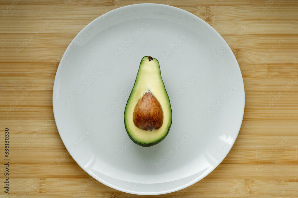 A half of fresh green avocado isolated in the middle on the plate on wooden table top view. Closeup. A half of fresh green avocado isolated in the middle on the plate on wooden table top view. Closeup.