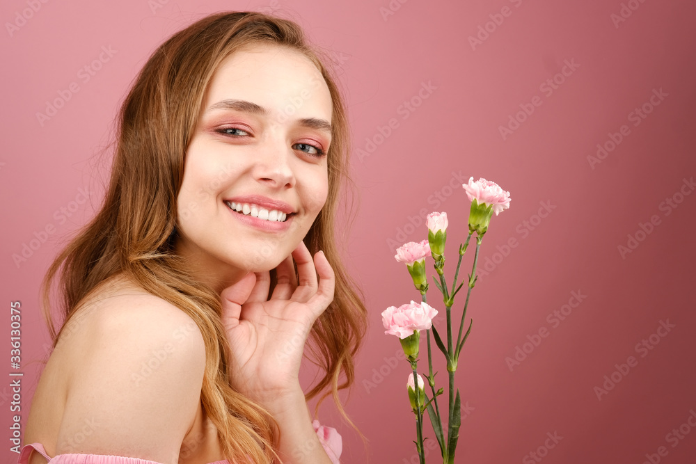 Close-up beauty portrait of an attractive young woman in a summer dress holding a carnation flower in her hand. A girl with light wavy hair. Isolated on a pink background Close-up beauty portrait of an attractive young woman in a summer dress holding a carnation flower in her hand. A girl with light wavy hair. Isolated on a pink background
